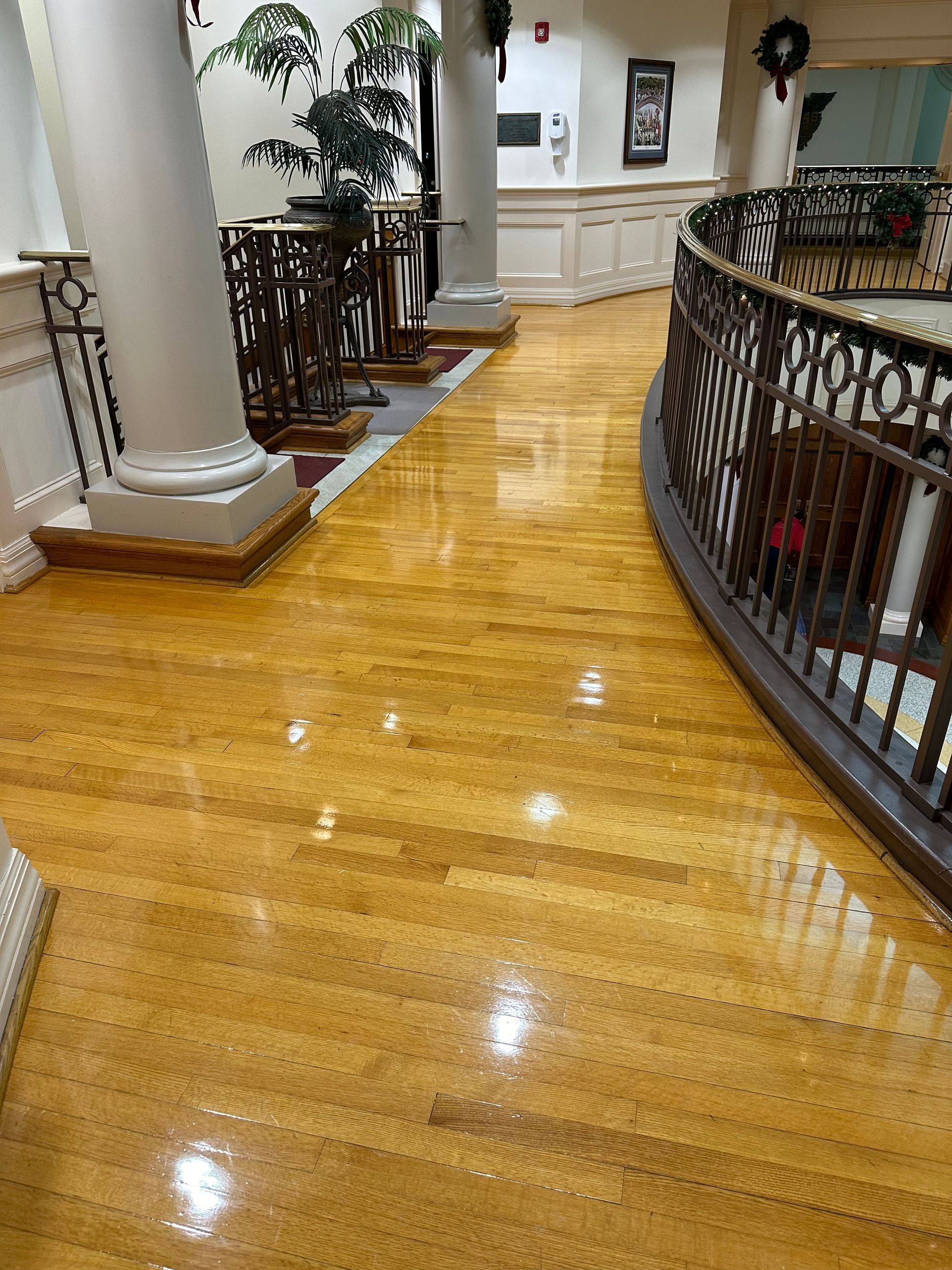 A glossy, golden-brown hardwood hallway floor curves past white columns and a dark metal railing in a decorated interior.