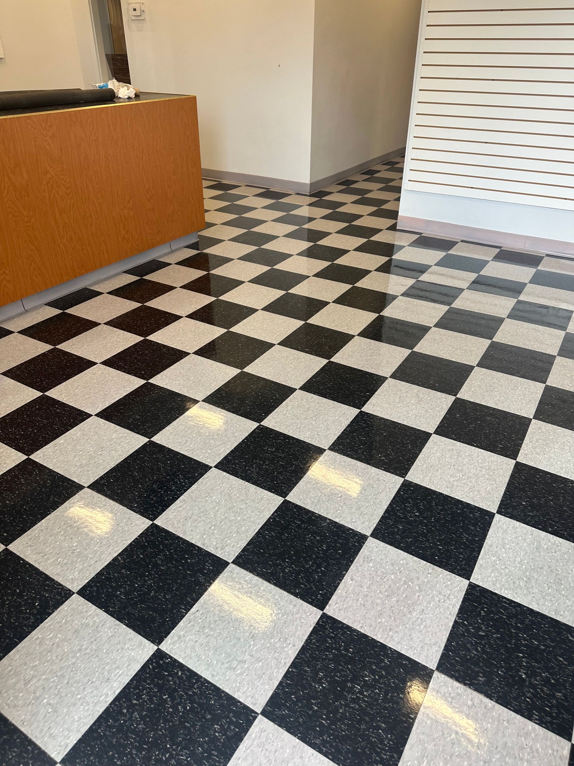 An indoor view of a floor with a glossy black and white checkered tile pattern, leading toward a counter and white wall.
