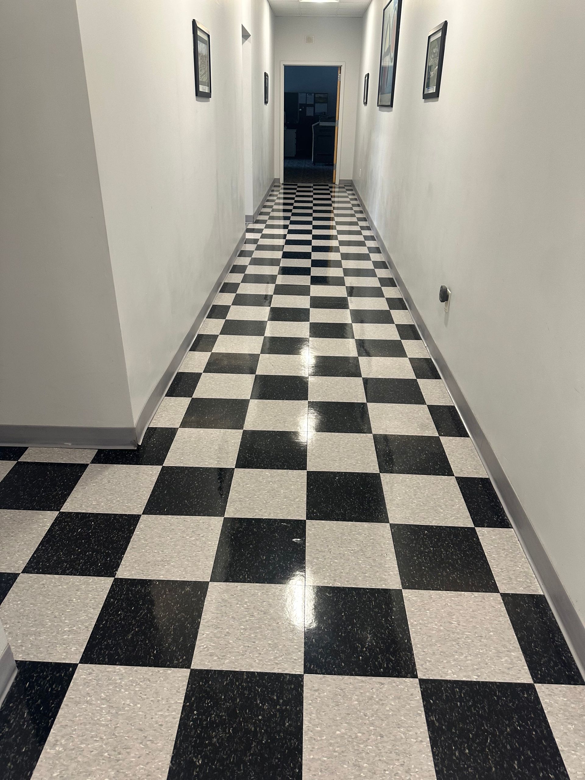 A hallway with black and white checkered tile flooring, white walls, and framed pictures on both sides.