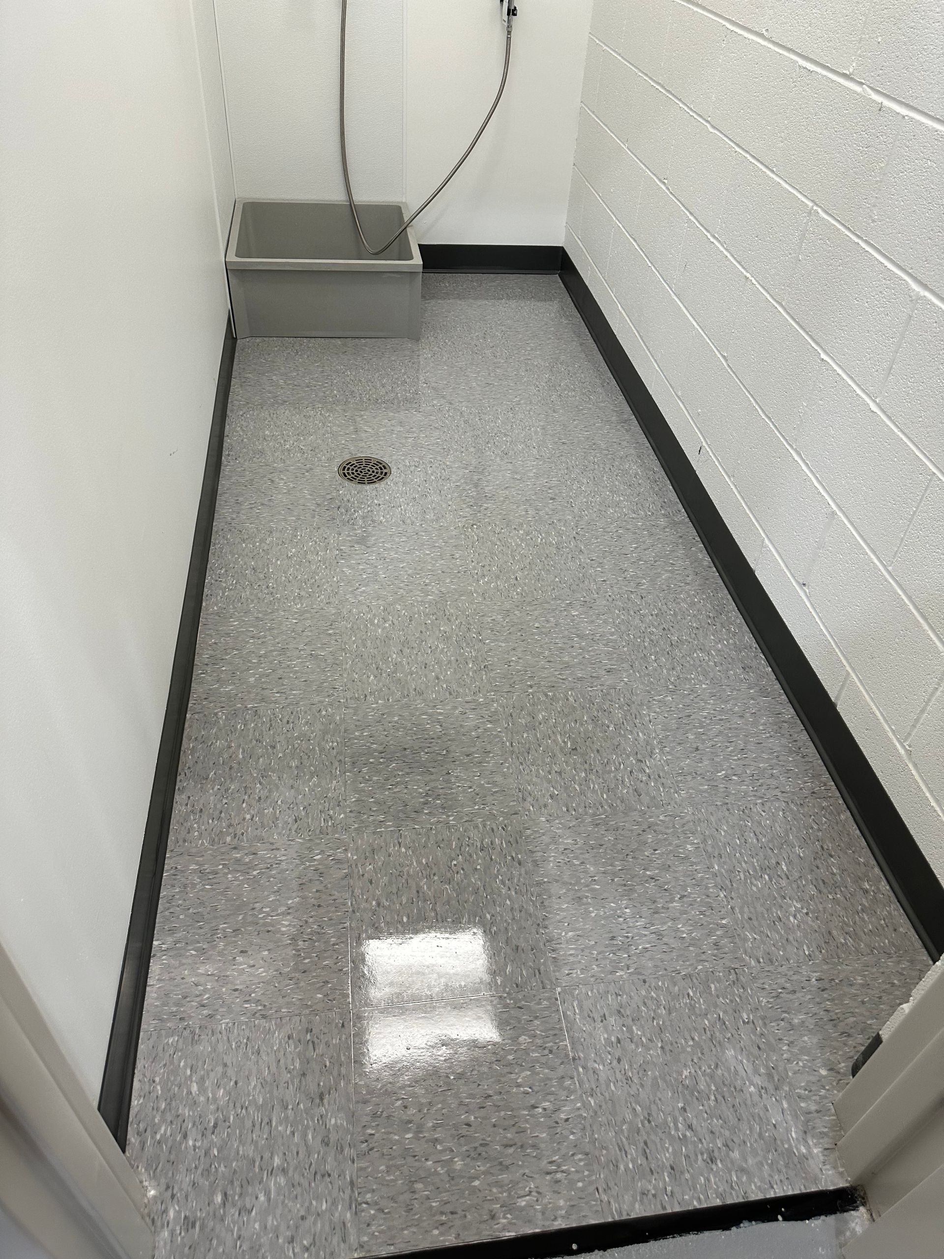 A narrow utility room with gray speckled epoxy flooring, white walls, a floor drain, and a wall-mounted basin.