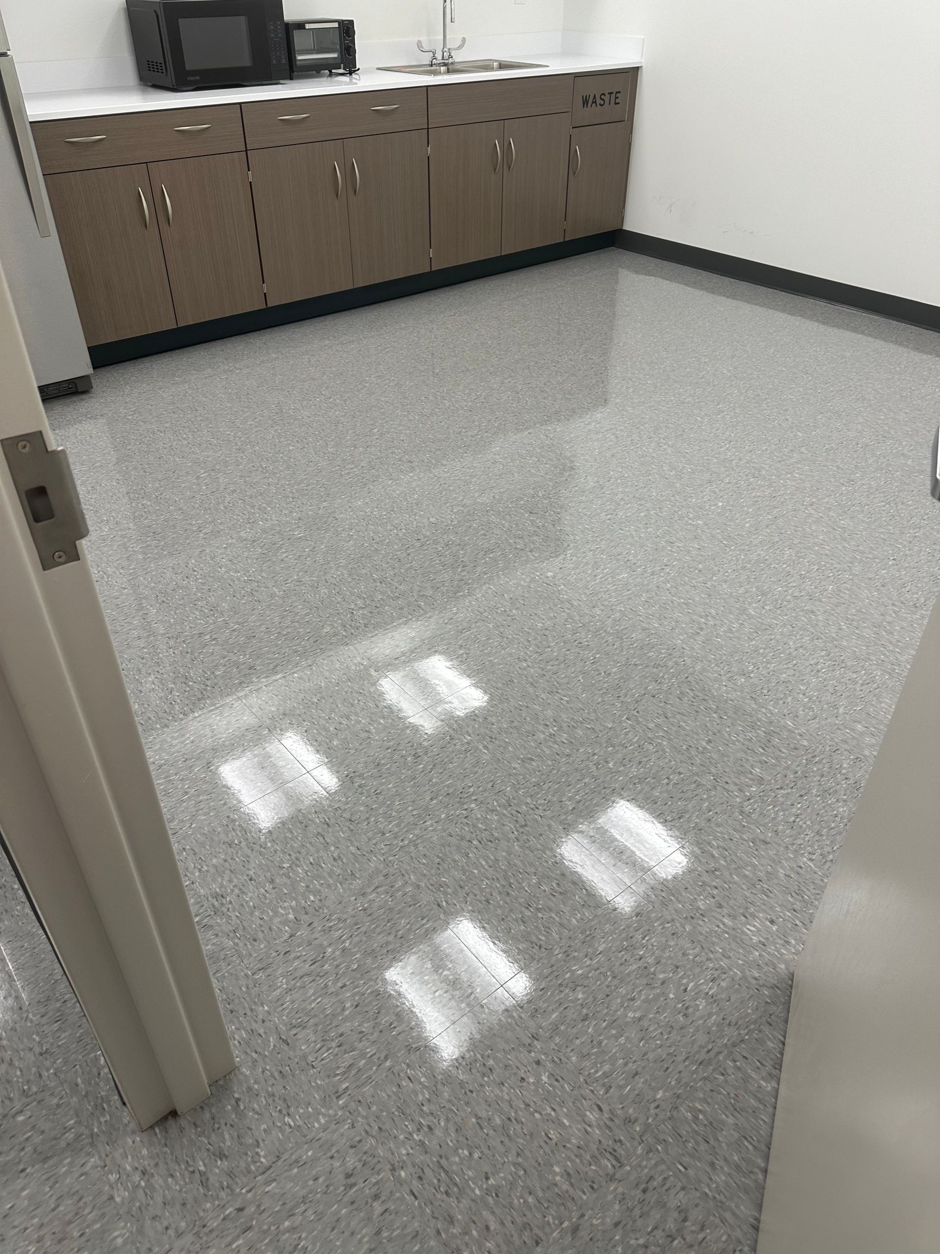 A bright, empty breakroom with a speckled gray epoxy floor, brown cabinets, and a microwave on the counter.