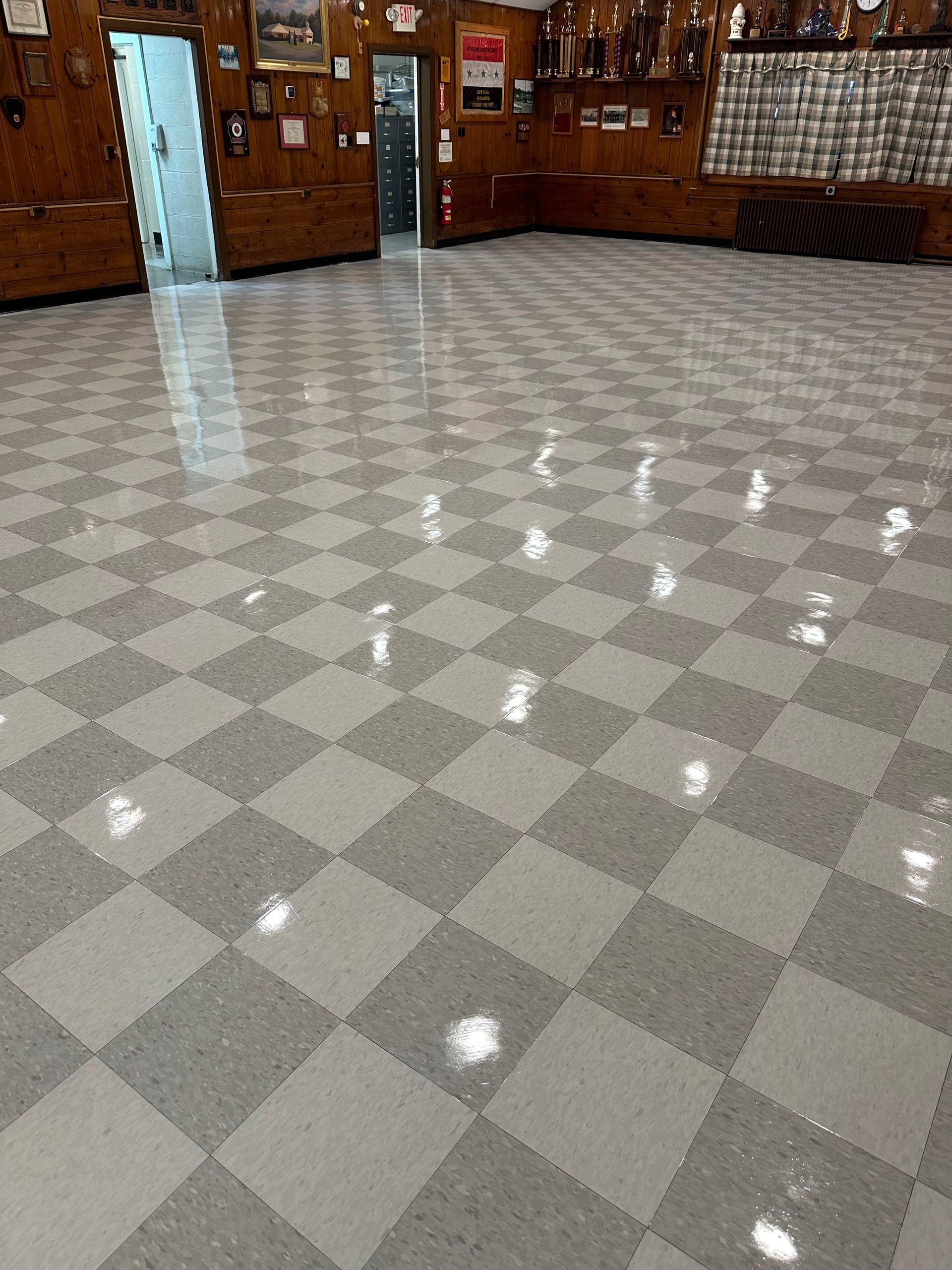 A spacious room with wood-paneled walls and a shiny, grey and white checkerboard tile floor.