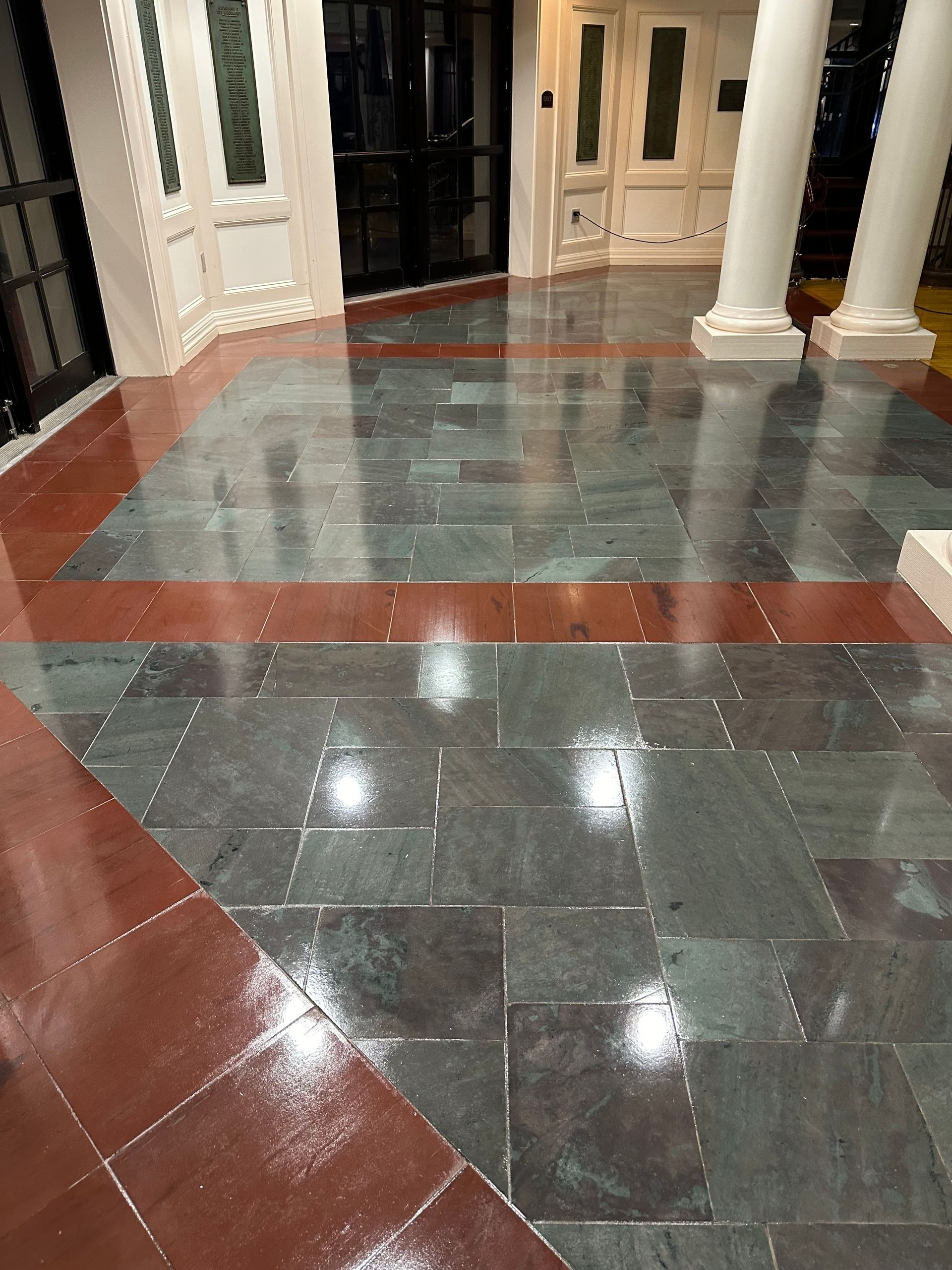 Shiny floor made of dark gray stone tiles arranged in a grid with wide, red-orange stone border accents.
