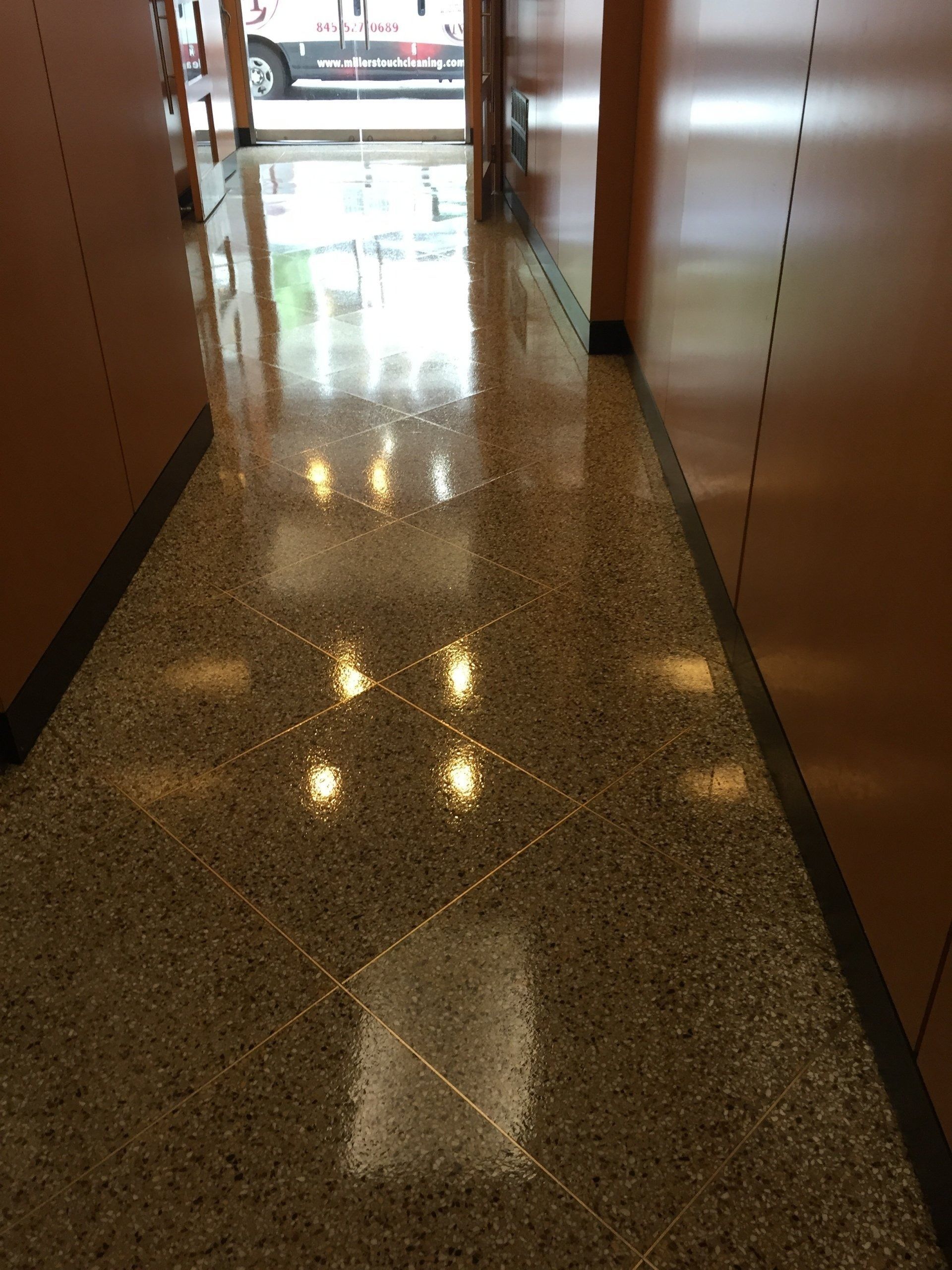 A polished, speckled tile hallway with reflections of overhead lights, leading to a doorway at the end.
