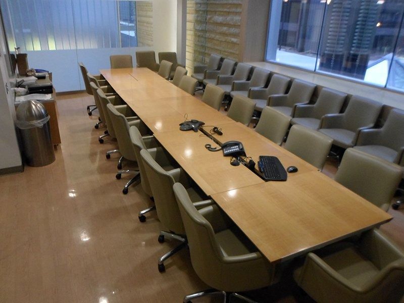 A long conference table with beige chairs in a brightly lit, modern office room.