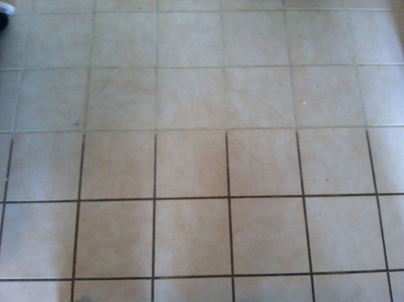 A floor of square, light-colored ceramic tiles with dark grout lines, showing a visible difference in cleanliness.