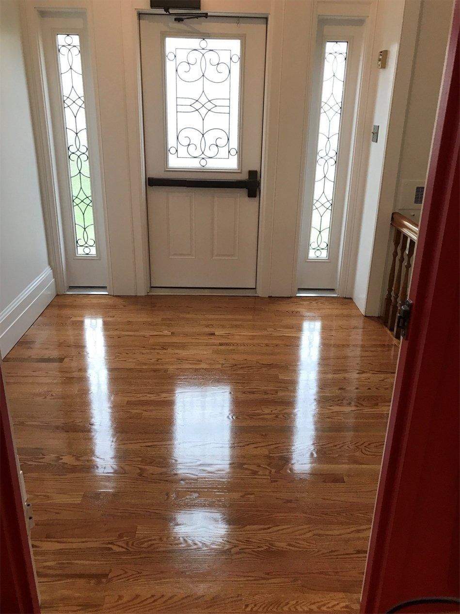 A brightly lit entryway with polished wood floors, a white front door with a decorative glass panel, and two sidelights.