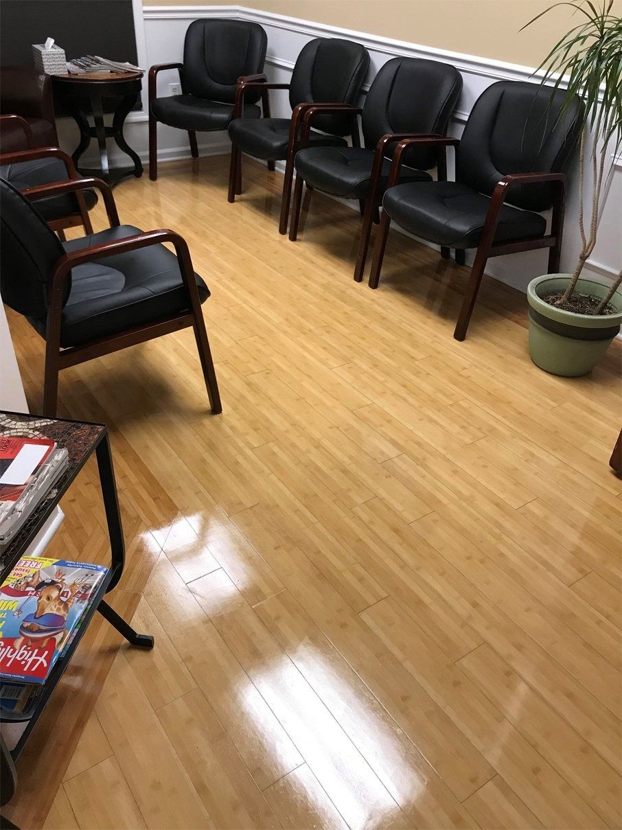 A waiting room with five black chairs arranged along the wall, light wood flooring, and a small plant in the corner.