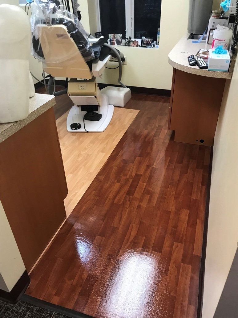 A dental office featuring a patient chair with a plastic cover, light wood flooring, and a countertop with supplies.
