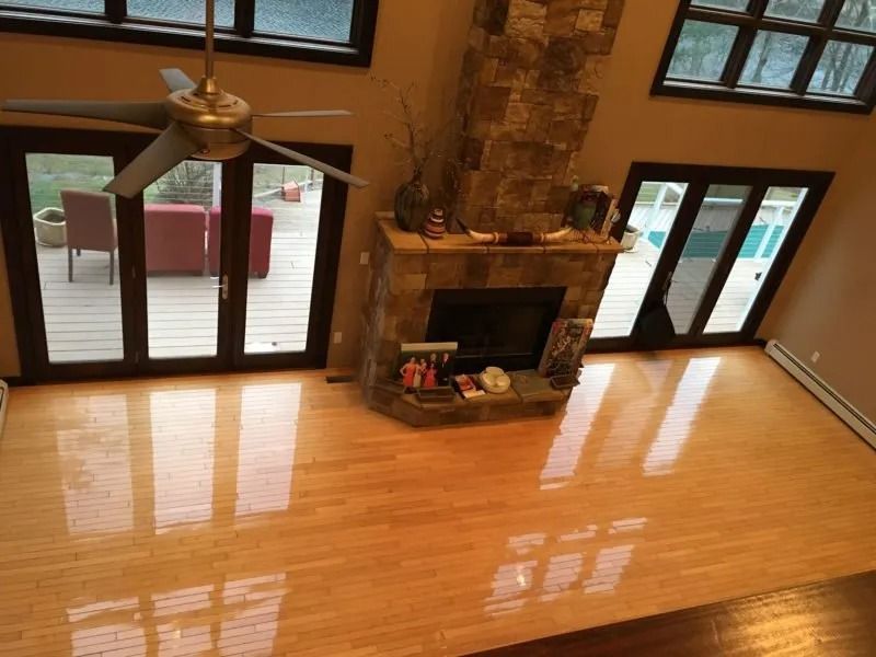 High-angle view of a living room with glossy light wood floors, a stone fireplace, and floor-to-ceiling glass doors.