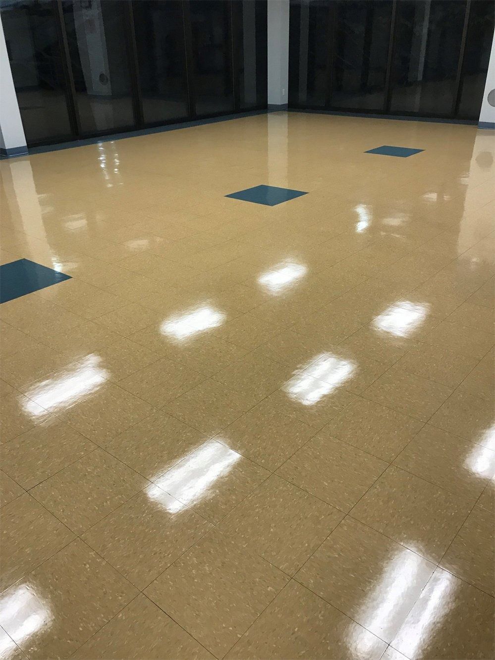 A bright, clean room with polished beige tile flooring featuring occasional dark teal accent tiles and reflective lights.