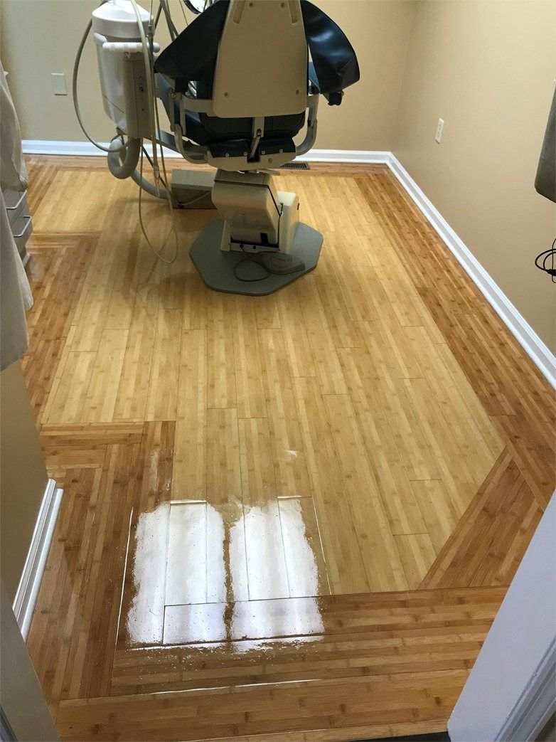 A dental exam room with a chair on light wood floors, featuring two distinct white rectangular floor patches.