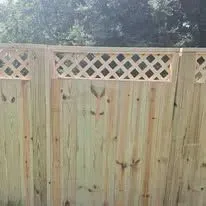 Wooden fence with lattice top against a backdrop of green trees.
