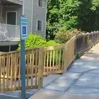 A wooden ramp with handrails leads to an accessible parking space. An accessible parking sign is posted nearby.