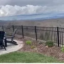 Black fence overlooking a landscape. Two chairs on a patio. Cloudy sky.