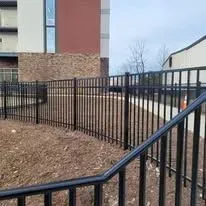 Black metal fence in front of a building with brown brick and brown mulch.