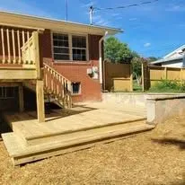 Wooden deck with stairs next to a house, surrounded by yard.