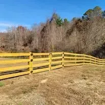 Yellow wooden fence in a field with trees and a blue sky in the background.