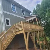 Wooden deck and stairs attached to a light green house with a window.