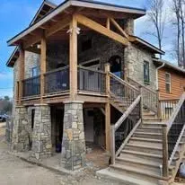 Rustic stone cabin with wooden deck, staircase, and covered porch.