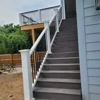 Outdoor staircase with white railings and black balusters leading up to a deck.