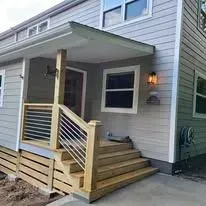 A wooden ramp and porch with a handrail leading to the front door of a gray-sided house.