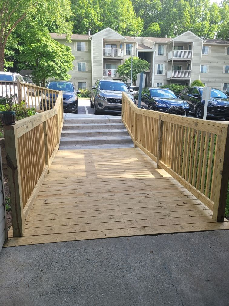 Wooden ramp with railings leading up to concrete stairs at an apartment complex. Cars are parked nearby.