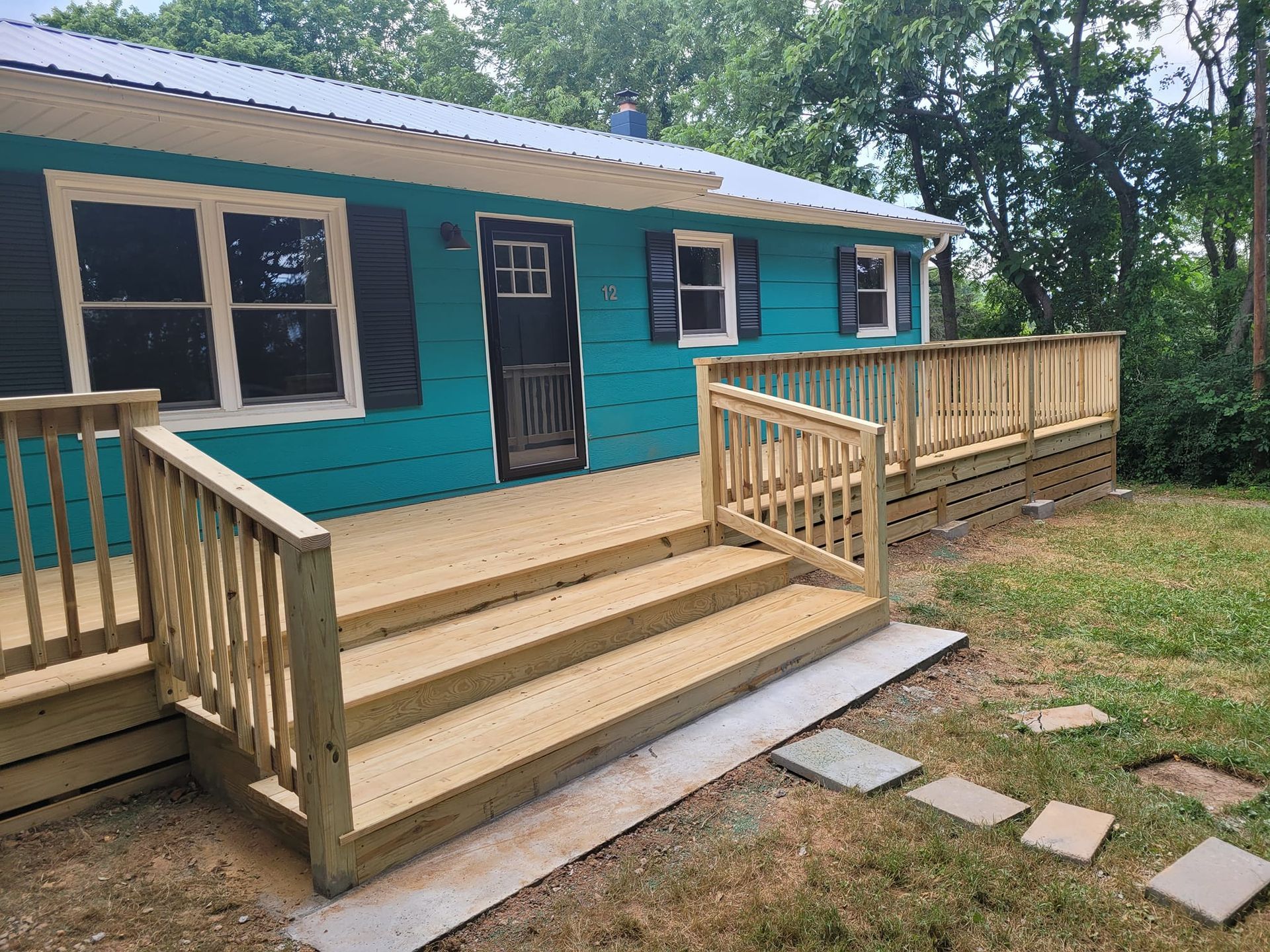 Teal house with wooden deck, stairs, and railing. Brown and grey accents in a grassy yard.