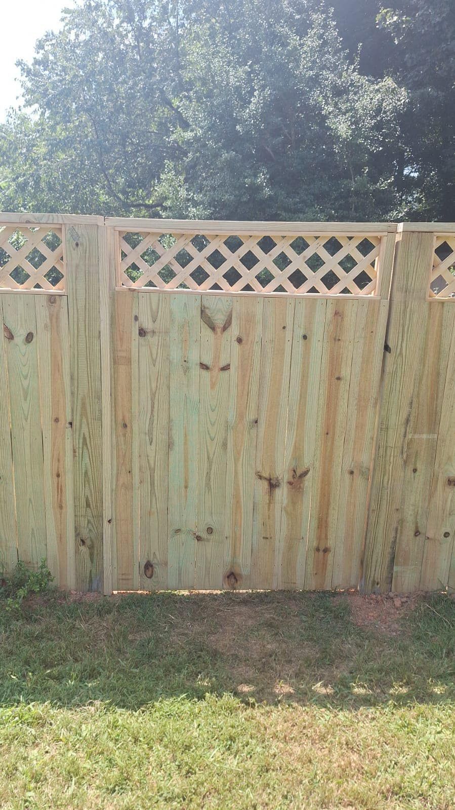 Wooden fence with lattice top, in front of green grass and trees.