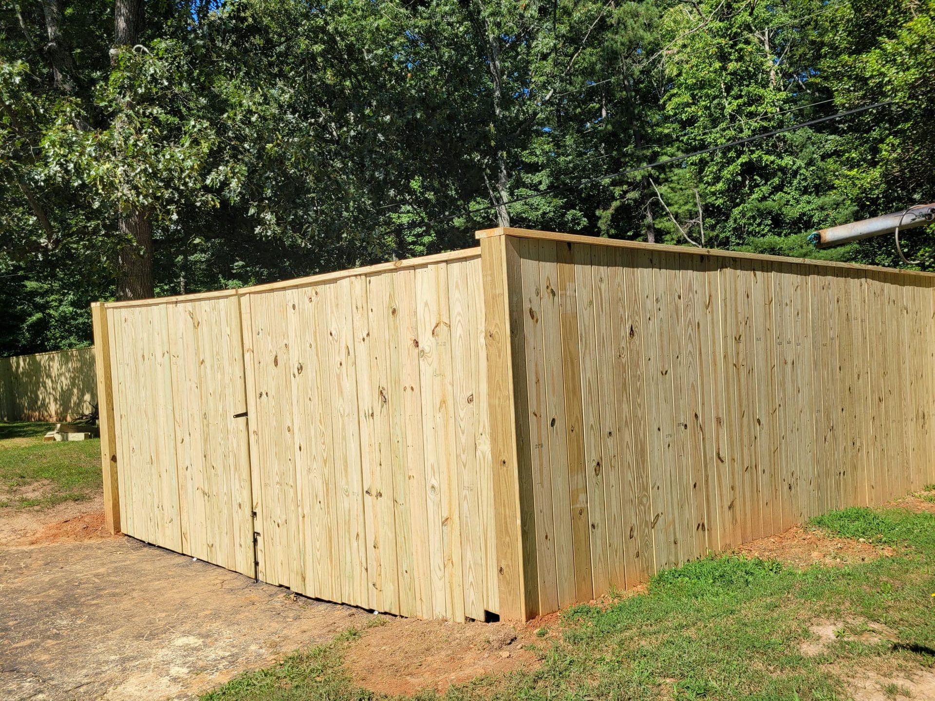 Wooden fence in a yard, bordering green grass and trees.