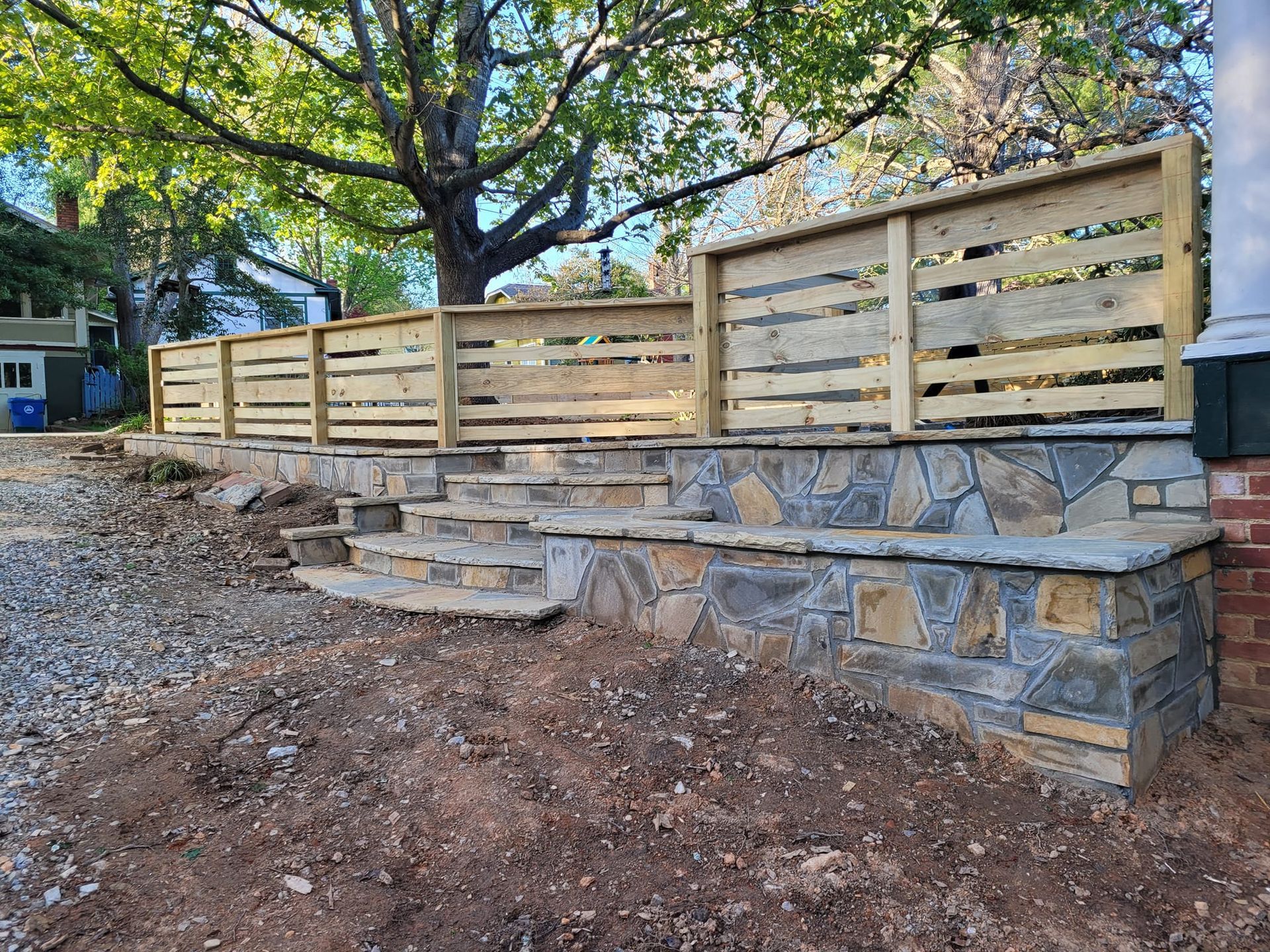 Stone wall with wooden fence, steps leading up. Brown and tan colors in an outdoor setting.