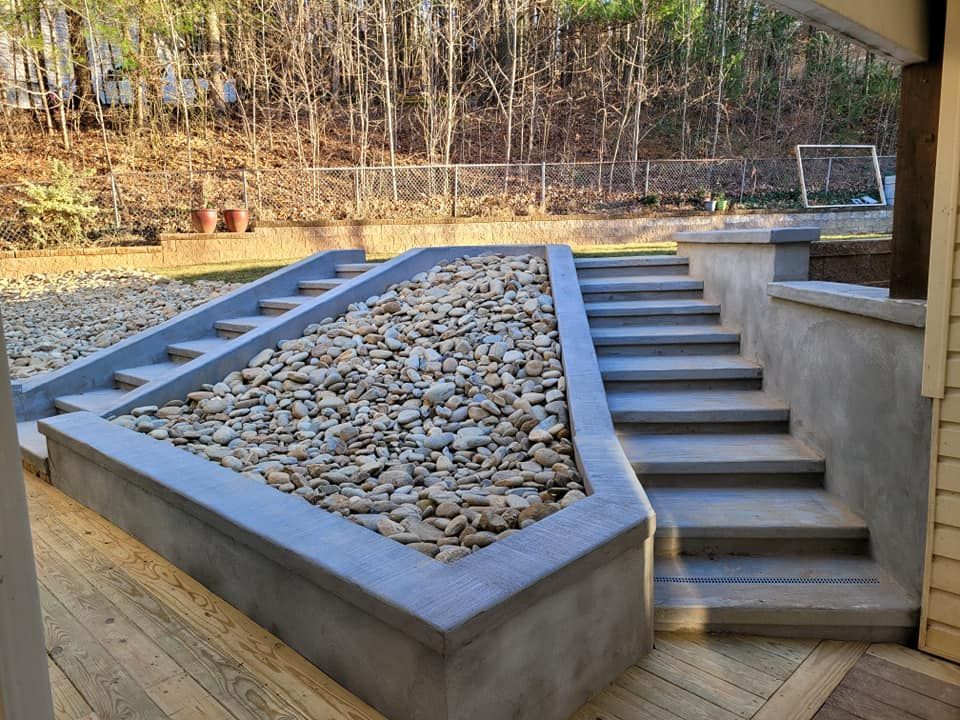 Concrete steps with a rock garden in the middle, leading up to a backyard with trees.