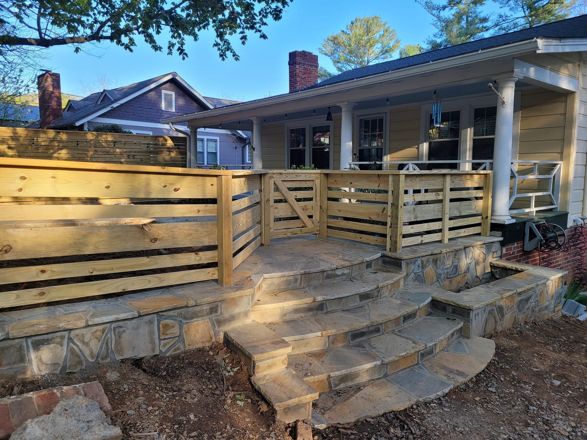 Stone steps lead to a wooden deck and home with a porch. Sunny outdoors.