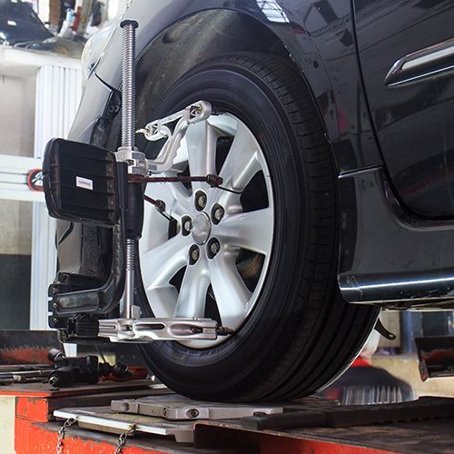 Wheel alignment machine adjusting a black car’s front wheel in a garage.