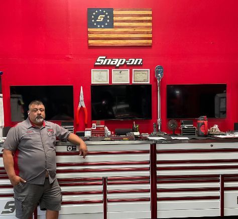 Man standing in a red Snap-on tool shop beside a counter with American flag decor and display cabinets