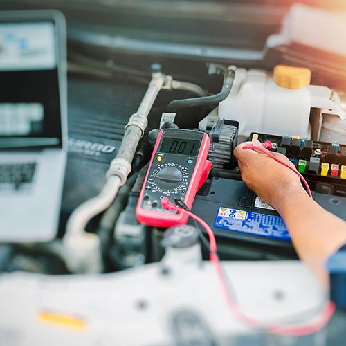 Technician testing a car battery with a multimeter in an engine bay