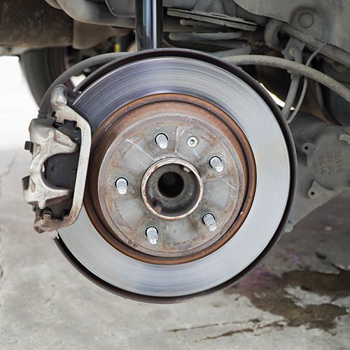 Car wheel hub and brake rotor with caliper, showing wear and rust near the axle