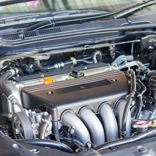 Close-up of a car engine bay with a black cover and silver intake manifold.