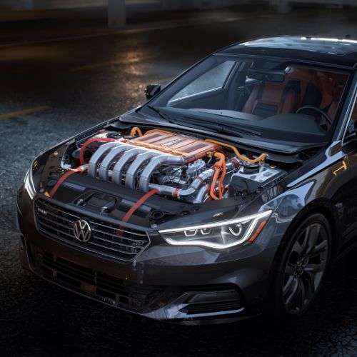 Black Volkswagen sedan with exposed hybrid engine, parked on a wet street at night.