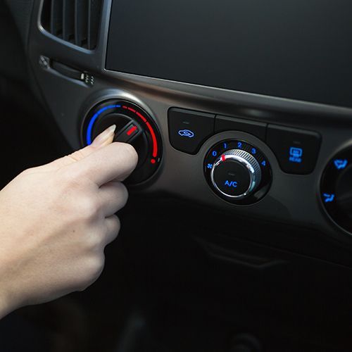 Hand adjusting a car’s climate control knob with illuminated blue and red dials