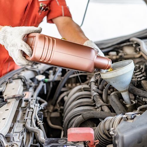 Mechanic pouring oil into a car engine with a funnel in a repair bay