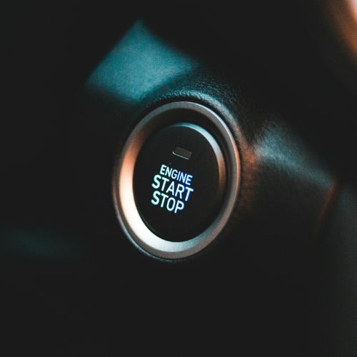 Close-up of a car engine start-stop button glowing blue and white on a dark dashboard