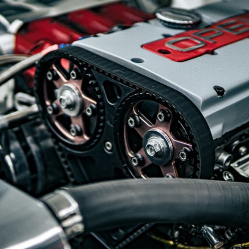 Close-up of a car engine with red and silver cover and visible timing belts and pulleys