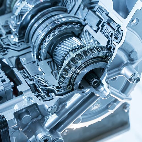 Close-up of a metallic gearbox with interlocking gears and shafts in a blue-tinted industrial setting