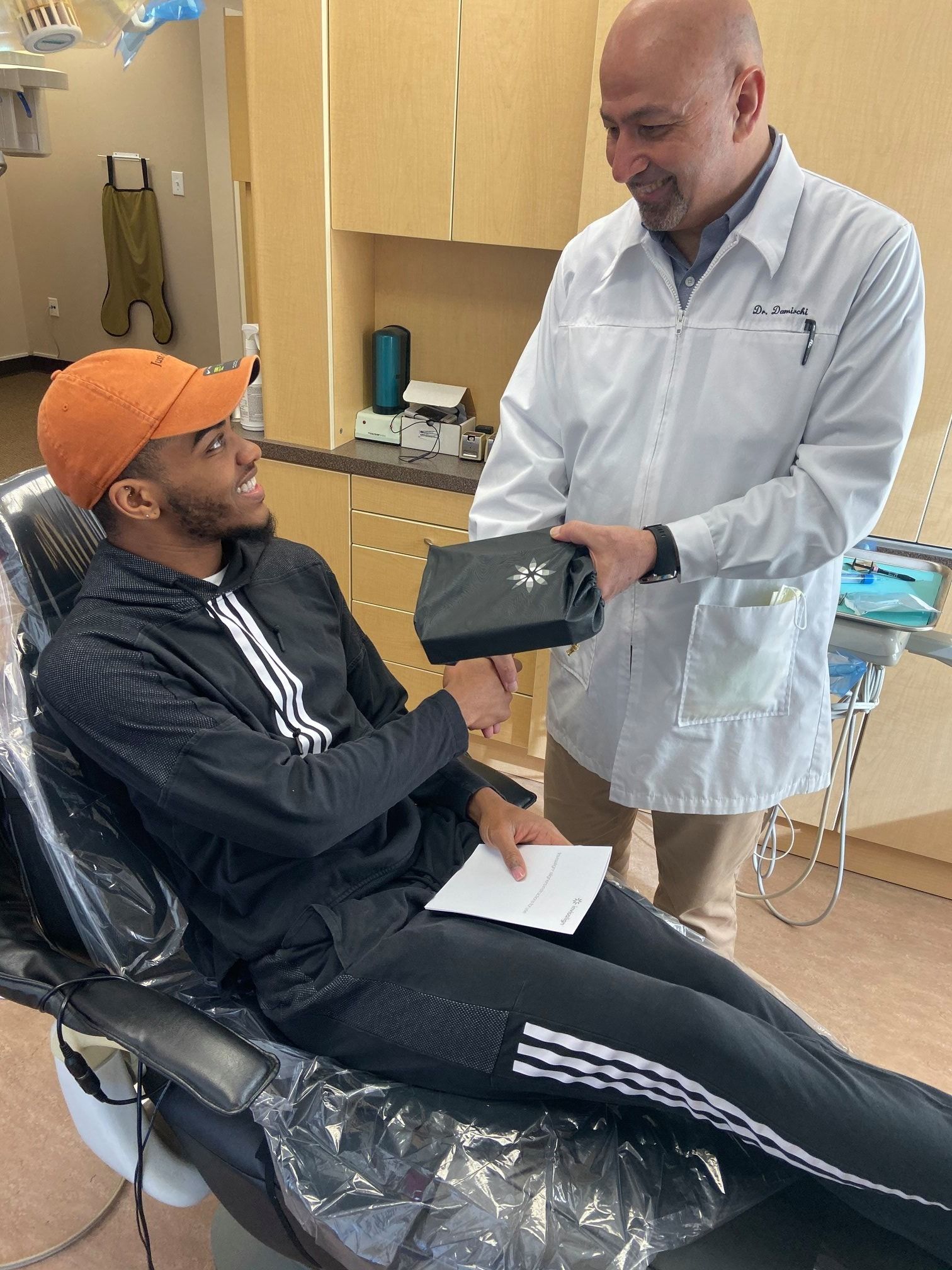 Man in dental chair shakes hands with dentist, who holds a device. Interior, clinic.