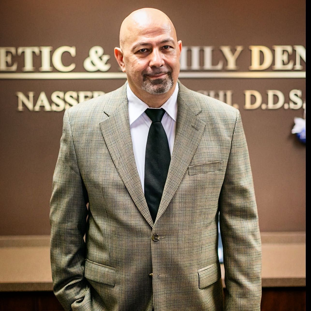 Man in a blazer and tie stands in front of a dentistry sign.