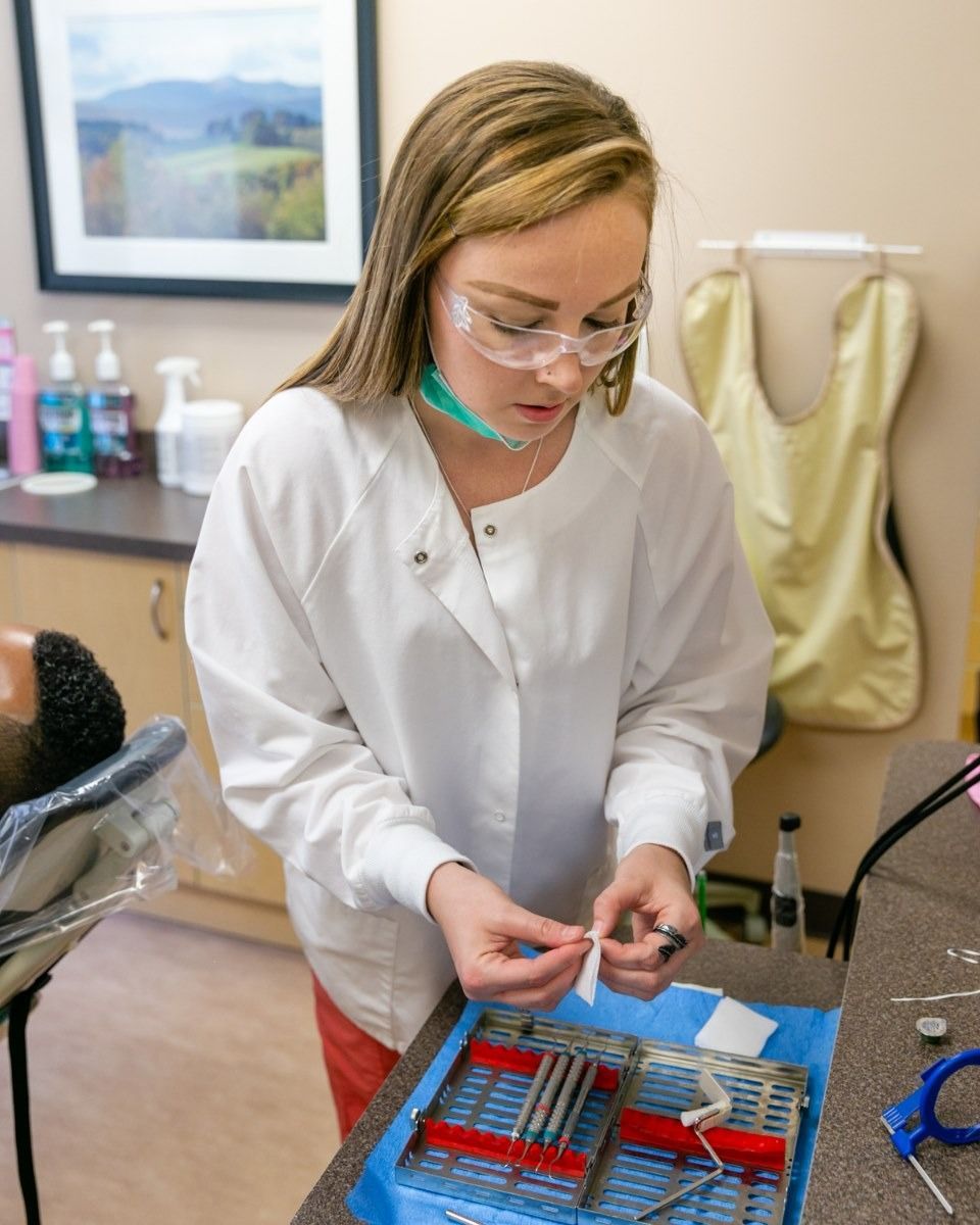 Dental assistant in protective eyewear and a lab coat prepares instruments in a dental office.