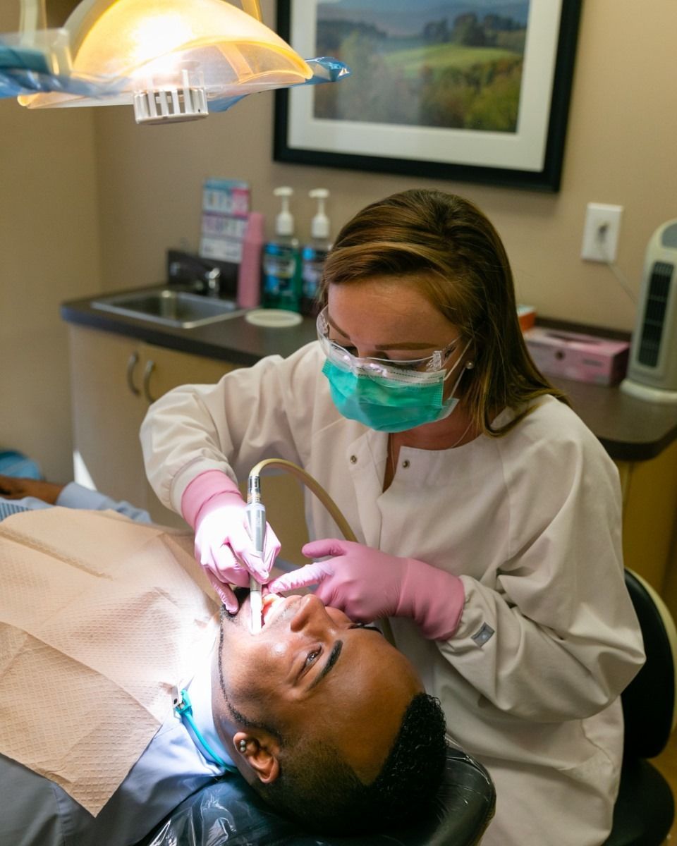 Dentist performing procedure on patient in a dental office. Patient reclined, wearing bib. Dentist wears mask, gloves.