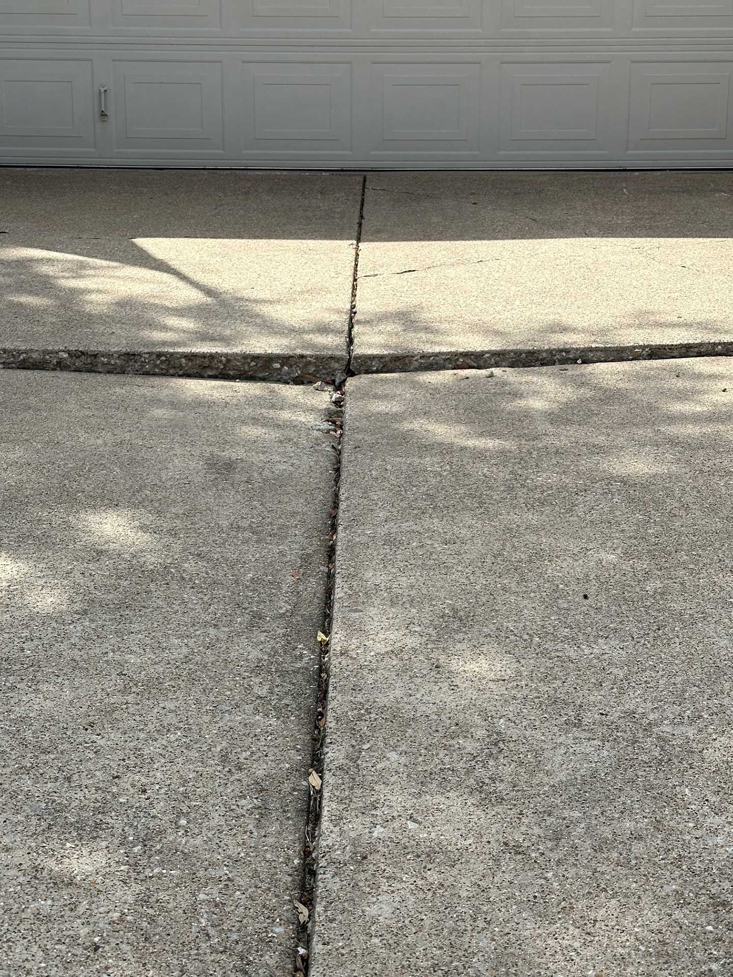 a close up of a cracked concrete driveway next to a garage door