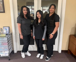Three women in black outfits stand indoors in front of a doorway.